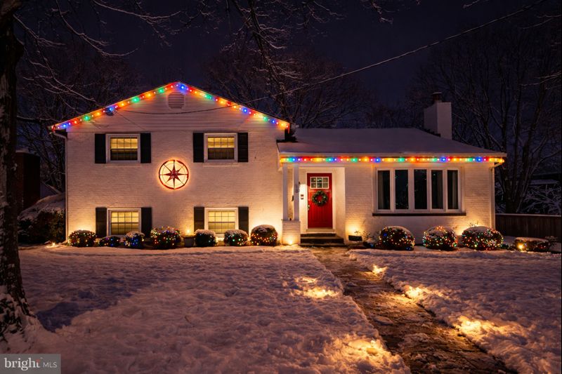 White house with multicolor roofline lights, star decoration, and pathway lighting in the snow